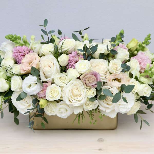 Low centerpiece of ivory roses and blush flowers in a wide gold container