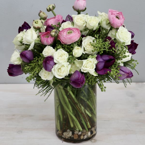 White roses with pink ranunculus and purple blooms in a clear glass vase