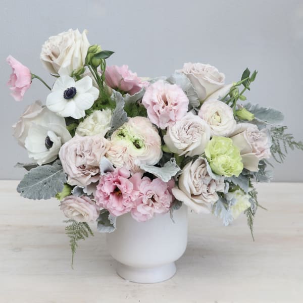 Pastel arrangement of roses, ranunculus, and anemones in a white pedestal vase