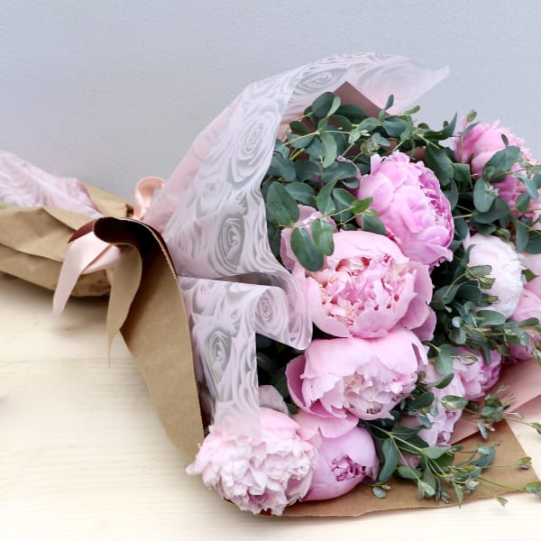 Bouquet of pink peonies wrapped in kraft paper and pink patterned cellophane