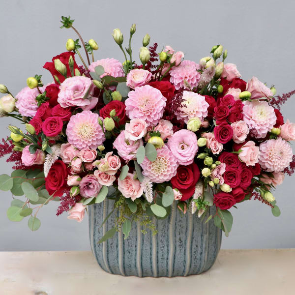 Lush pink and red flower arrangement in a textured blue ceramic container