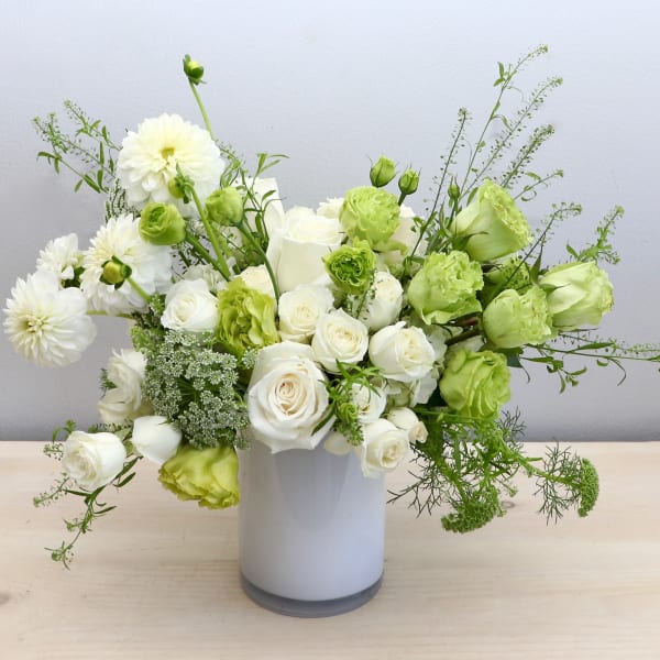 Asymmetrical white and green flower arrangement in a white cylinder vase