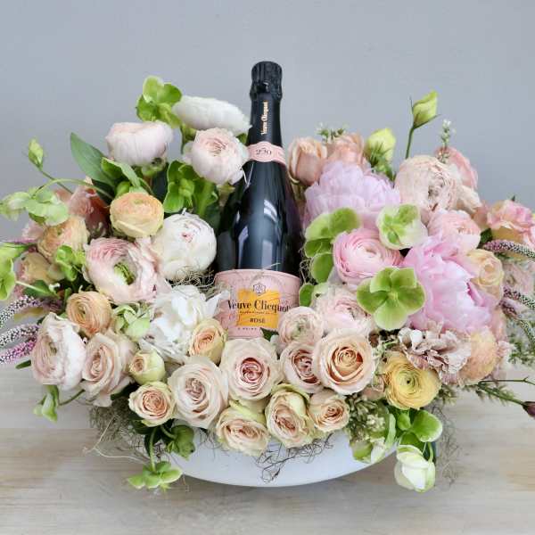 Low pastel flower arrangement in a white bowl with a pink champagne bottle in the center