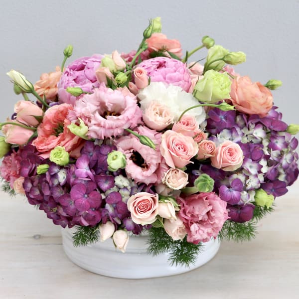 Low arrangement of pink and purple flowers in a white ceramic bowl