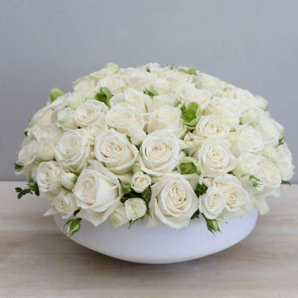 Low dome arrangement of cream white roses tightly packed in a round white bowl
