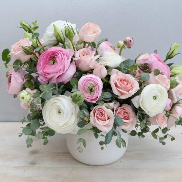Low white pot filled with pink and white ranunculus and roses in a loose, rounded arrangement