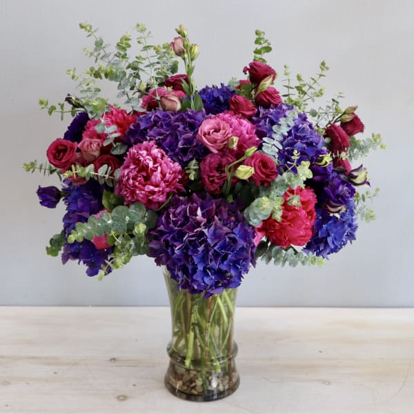 Tall arrangement of purple hydrangeas and pink roses in a clear glass vase