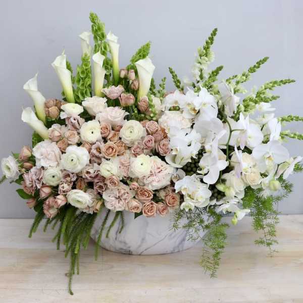 Low marble container filled with blush roses, white ranunculus, calla lilies, and cascading white orchids