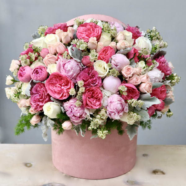 Pink and white roses and peonies arranged densely in a round pink hatbox-style container