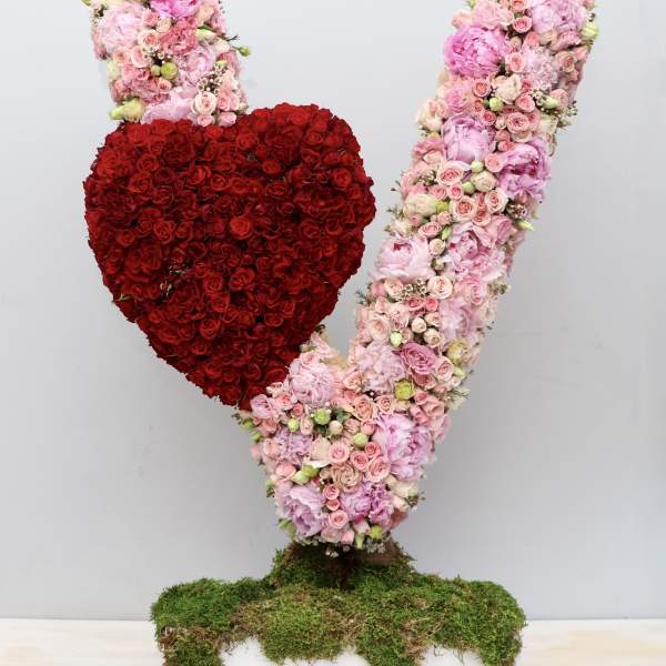 Tall pink floral V sculpture with a red rose heart on a moss-covered rectangular base