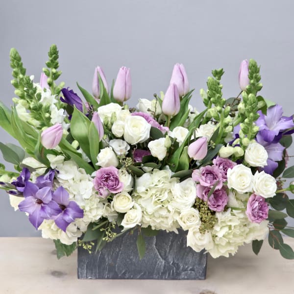 Rectangular arrangement of white and lavender flowers, including tulips and roses, in a gray stone container