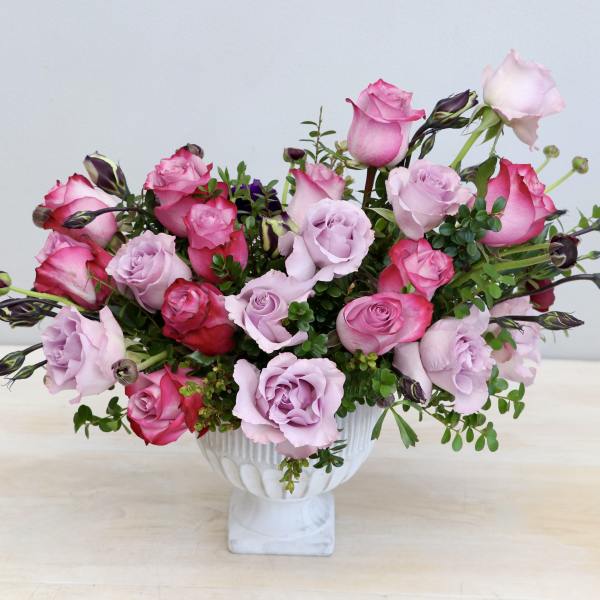Low pink and lavender rose arrangement in a white pedestal bowl