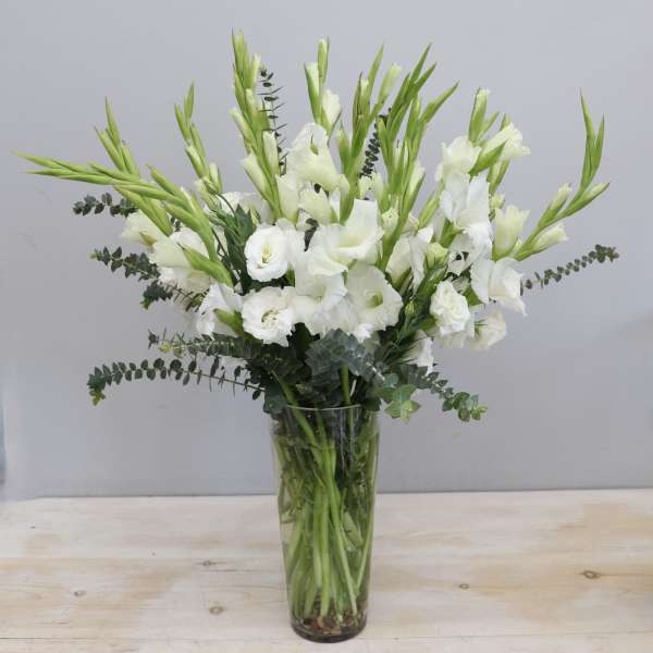 Tall arrangement of white gladiolus and lisianthus in a clear glass vase