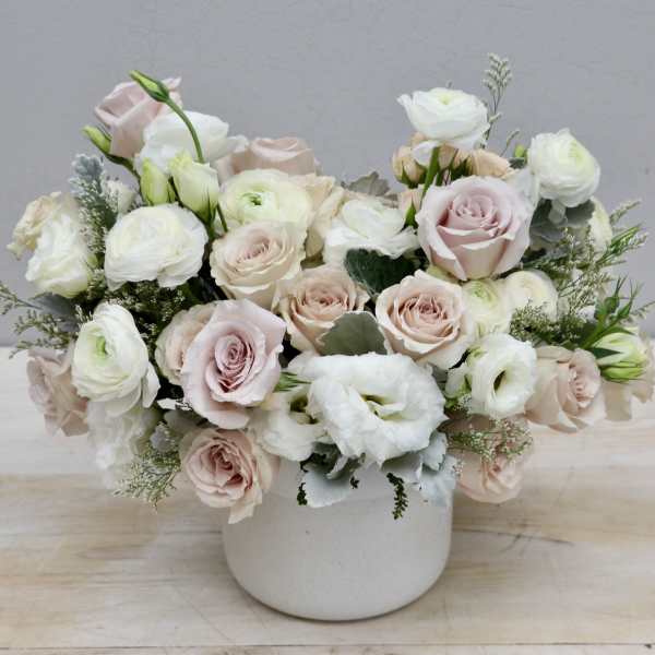 Low arrangement of blush roses and white ranunculus in a matte white ceramic pot