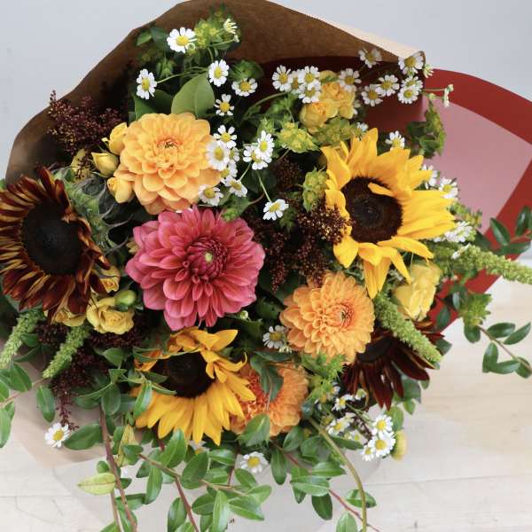 Bright bouquet with sunflowers, dahlias, spray roses, and small daisies wrapped in brown paper