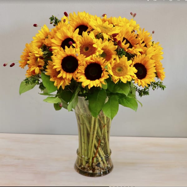 Tall bouquet of yellow sunflowers in a clear glass vase with visible stems