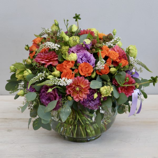 Low round arrangement of orange and purple flowers in a clear glass bowl vase