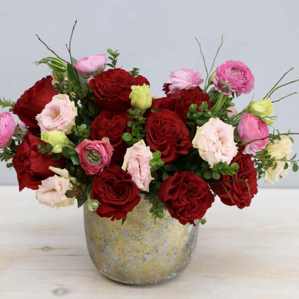 Low arrangement of red roses and pink blooms in a rustic gold-toned pot