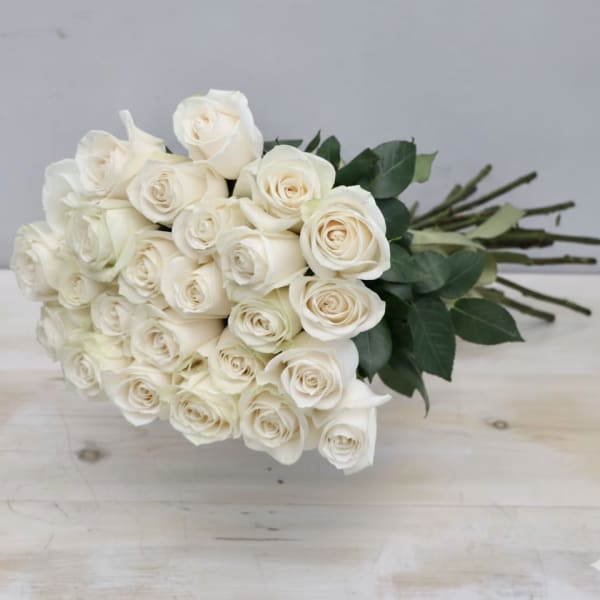 Hand-tied bouquet of long-stemmed ivory roses resting on a light wooden surface
