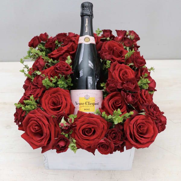 Bottle of rosé champagne surrounded by red roses in a white wooden box