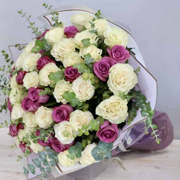 Large bouquet of cream and magenta roses with trailing eucalyptus, wrapped in white paper.