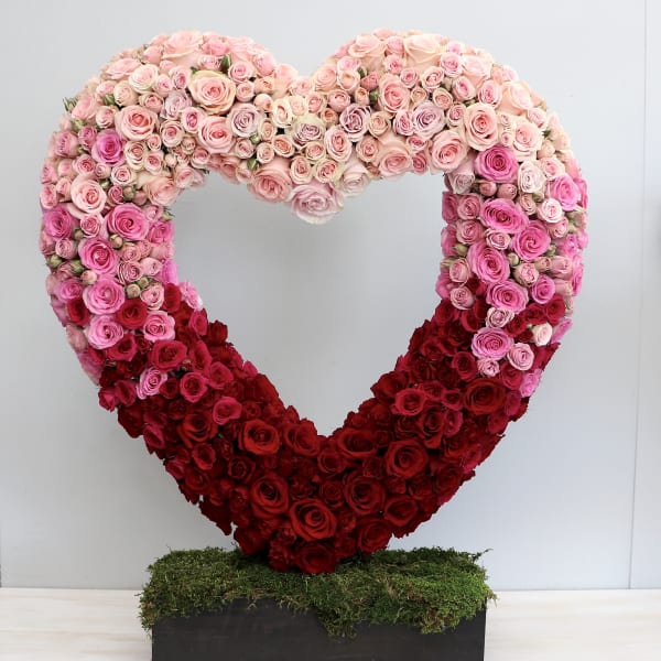 Large open heart of pink and red roses on a moss-covered base in a rectangular black container