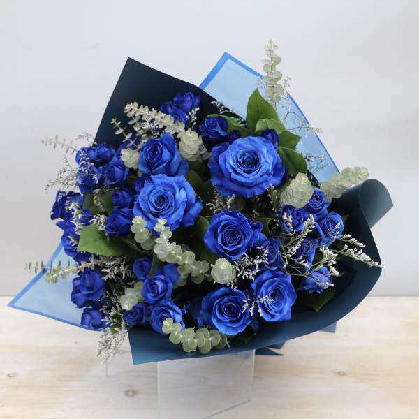 Hand-tied bouquet of vivid blue roses with silver eucalyptus in blue wrapping paper