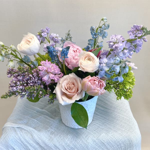 Pastel bouquet of roses, peonies, and blue-purple blooms in a white vase