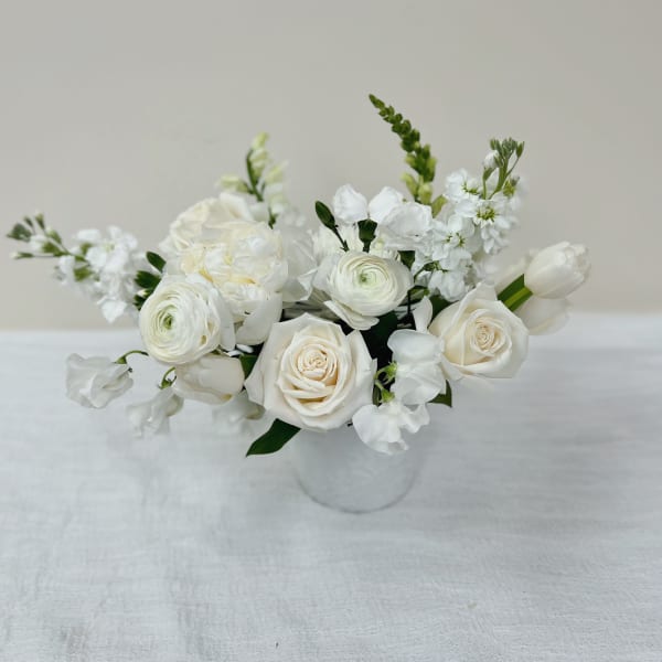 Low white arrangement of roses, ranunculus, tulips and other blooms in a small round vase