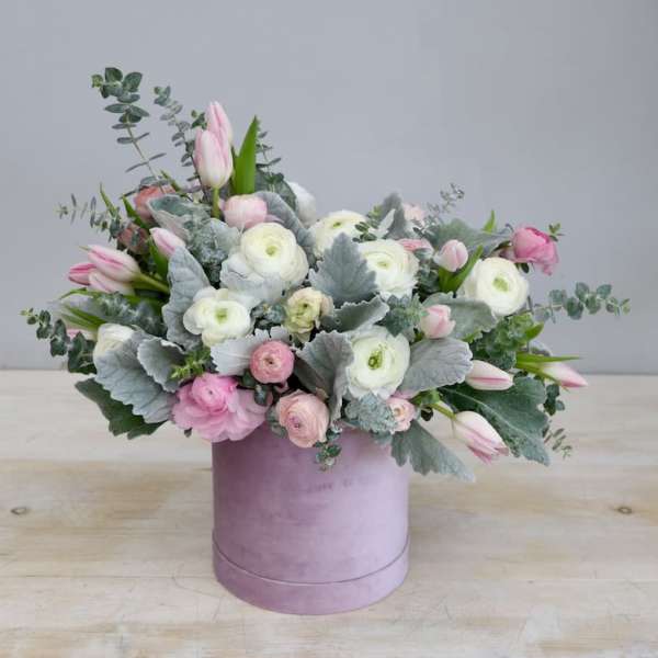 Pastel pink and white flower arrangement with silver foliage in a round lavender hatbox.