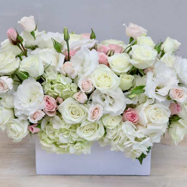 Low rectangular arrangement of white and pale pink roses and lisianthus in a white box.