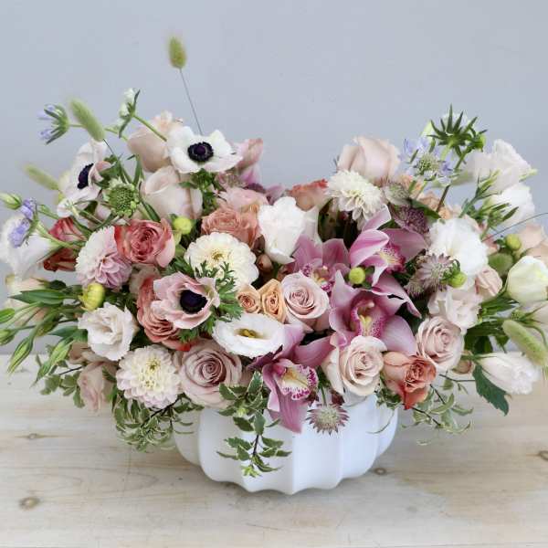 Low white bowl filled with pastel pink, peach, and white flowers including roses, orchids, and anemones.