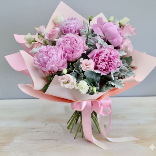 Hand-tied bouquet of pink peonies and pale lisianthus wrapped in pink paper with a satin ribbon
