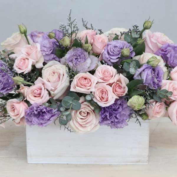 Low arrangement of pink roses and lavender lisianthus in a white wooden box