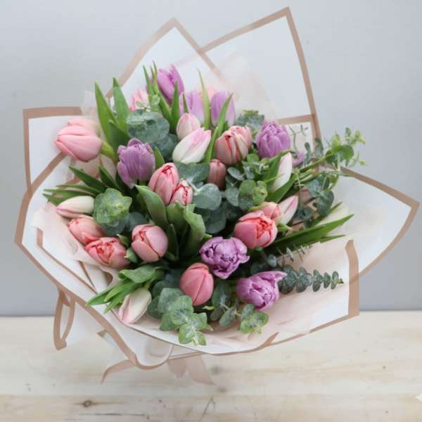Hand-tied bouquet of pink and purple tulips with eucalyptus wrapped in white and beige paper.