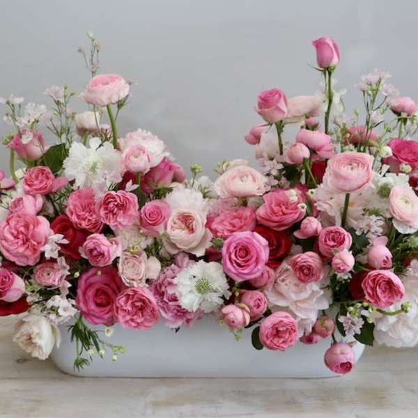 Low centerpiece of pink and white roses and ranunculus in a long white container
