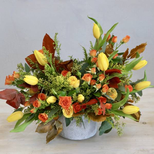 Low arrangement of yellow tulips and orange roses in a round white container