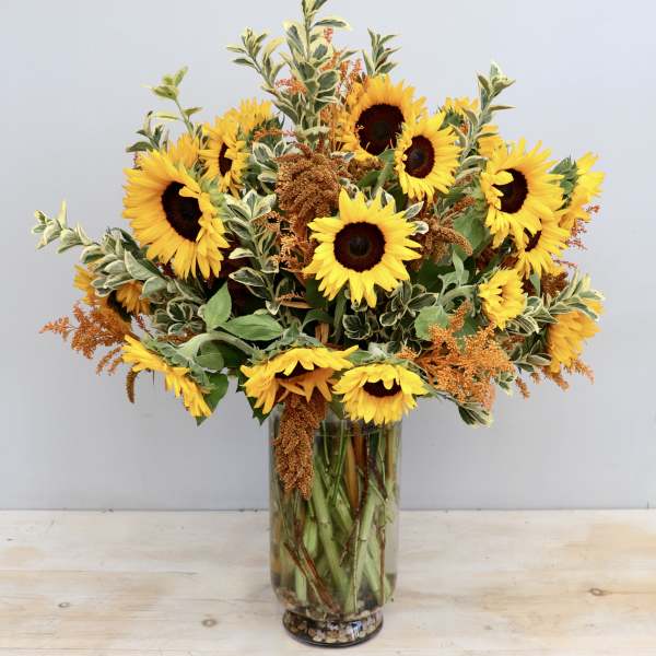 Tall glass vase of yellow sunflowers with orange filler blooms and variegated foliage