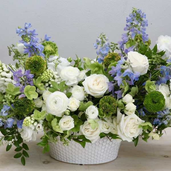 Low arrangement of white roses and ranunculus with blue flowers in a white ceramic bowl