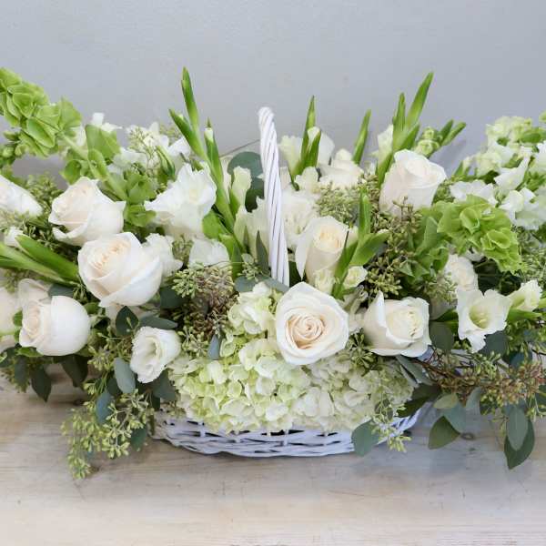 Low white and green floral basket with white roses, hydrangeas, and bells of Ireland