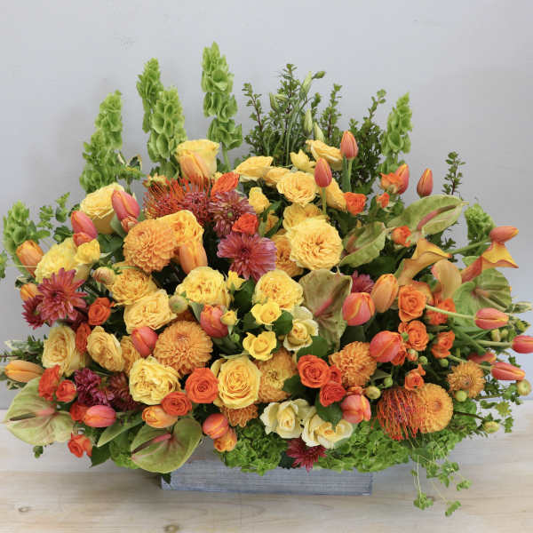Tall yellow and orange floral arrangement with roses, tulips, and mums in a rectangular container