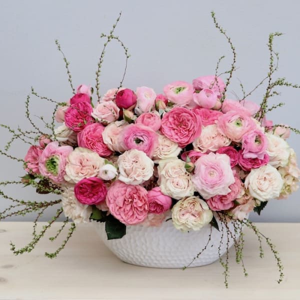 Low arrangement of pink and white roses and ranunculus in a white textured bowl