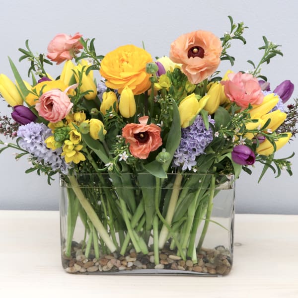 Colorful spring flower arrangement in a rectangular glass vase with river rocks