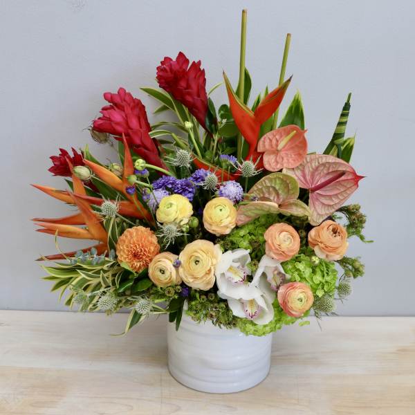 Colorful tropical flower arrangement in a white ceramic cylinder vase