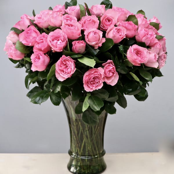 Tall bouquet of pink roses densely arranged in a clear glass vase