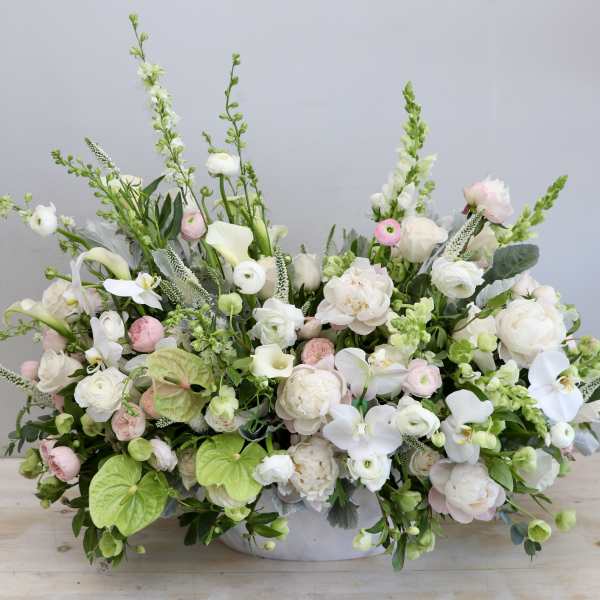 Low, wide arrangement of white and blush flowers with orchids and calla lilies in a white bowl