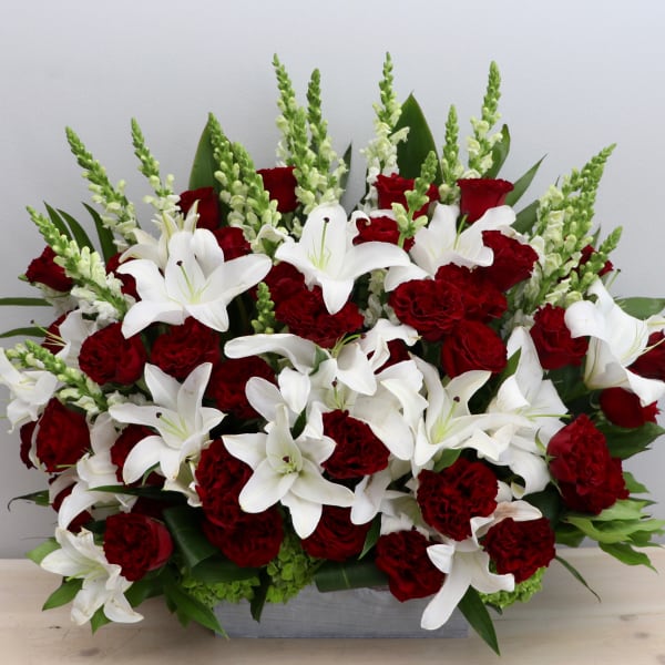 Red roses and carnations with white lilies and snapdragons in a low rectangular container