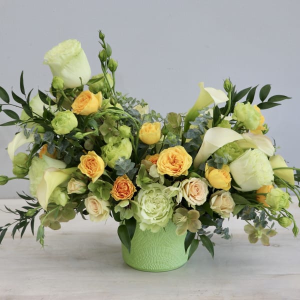 Low yellow and cream flower arrangement with roses and calla lilies in a green ceramic pot