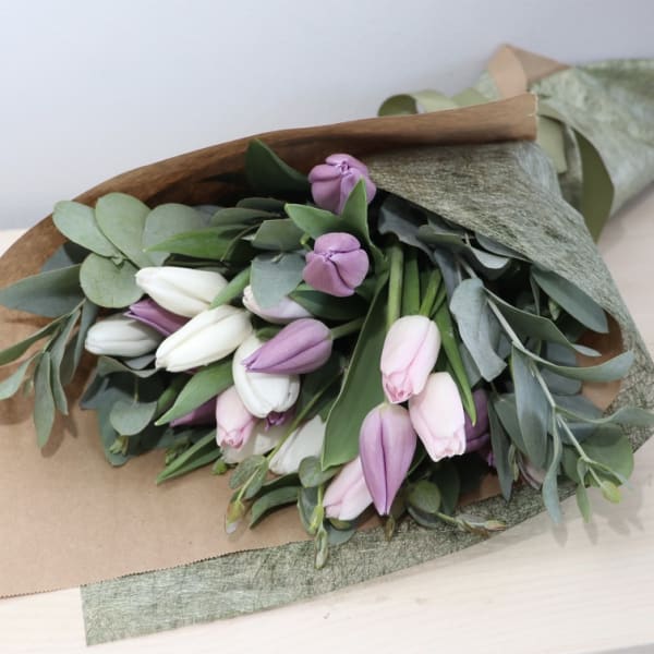 Hand-tied bouquet of white and pastel pink tulips wrapped in brown kraft and green paper.