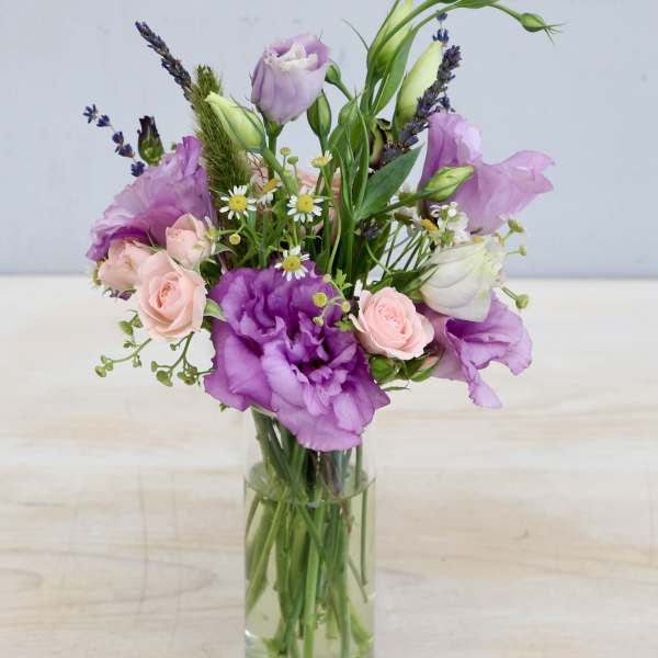 Tall glass vase with purple lisianthus, pink spray roses, and small white daisies in a loose arrangement